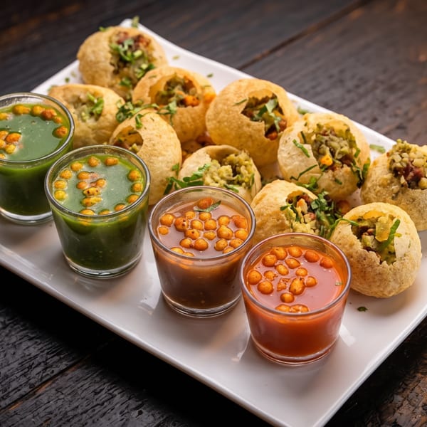 Crispy pani puri stuffed with spiced fillings, served with green and tamarind chutneys on a white platter.