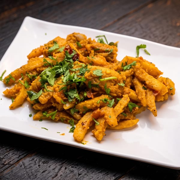 Golden-brown vegetable fritters piled on a white square plate and garnished with fresh cilantro.