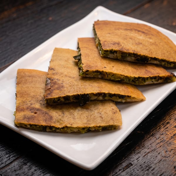 Four golden stuffed flatbreads, cut into rectangles, arranged on a white plate atop a rustic wooden table.
