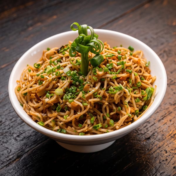 Bowl of stir-fried noodles garnished with chopped and curled green onions on a dark wooden table.